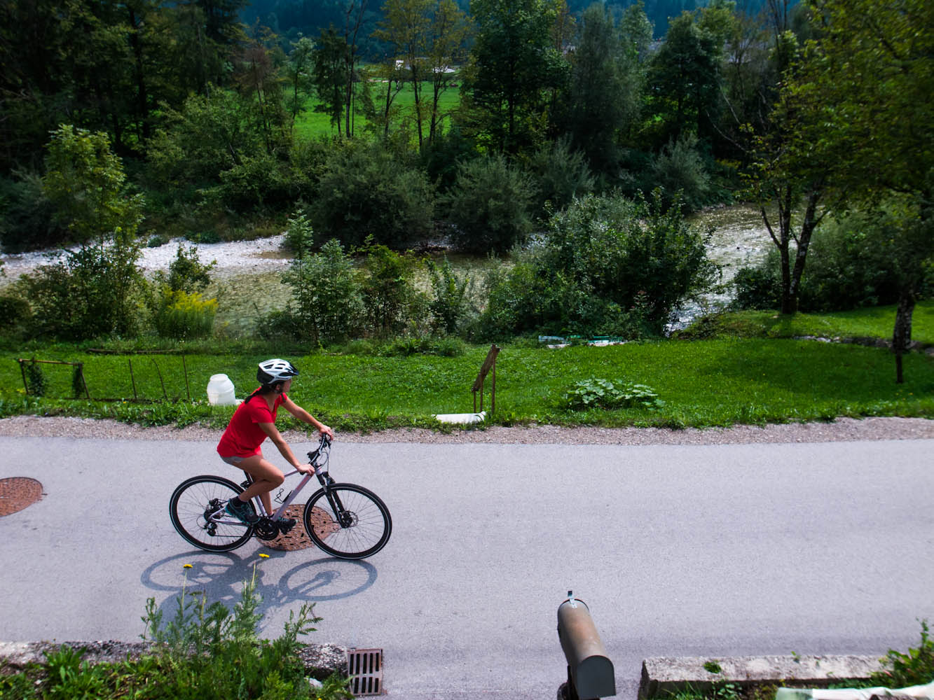 Een fietser rijdt over een rustig weggentje langs riviertje Sava Bohinjka in de vallei van Bohinj in Slovenië.
